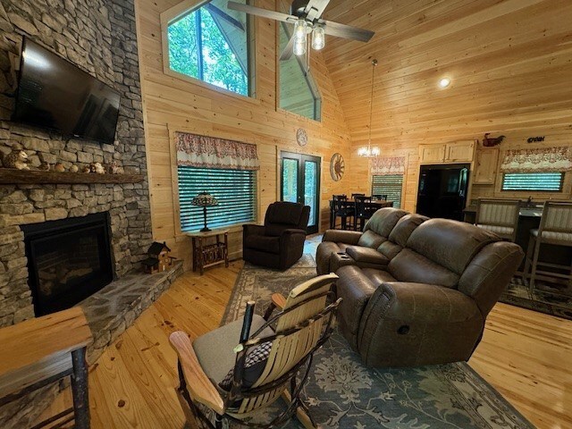 living room with light hardwood / wood-style flooring, wood walls, ceiling fan with notable chandelier, and high vaulted ceiling