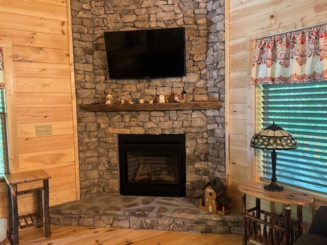 living room with wood walls, a stone fireplace, and hardwood / wood-style floors