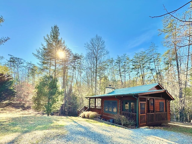 exterior space featuring driveway, metal roof, a chimney, and a lawn