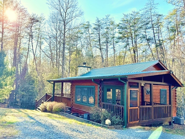 view of front facade featuring metal roof, a chimney, cooling unit, and log siding