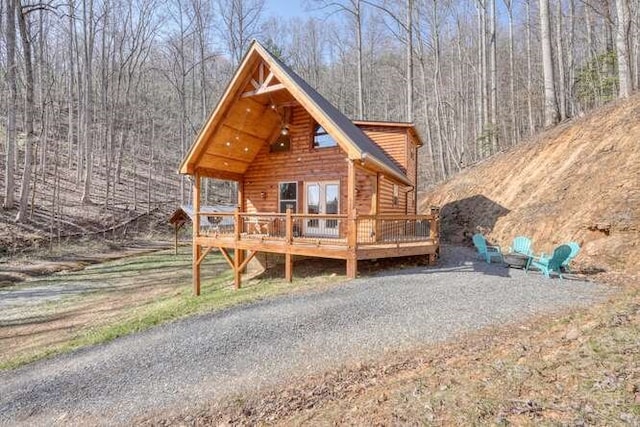 exterior space with driveway, a view of trees, and a deck