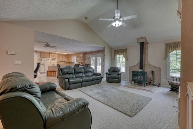 living room with ceiling fan, a wood stove, light carpet, a textured ceiling, and lofted ceiling