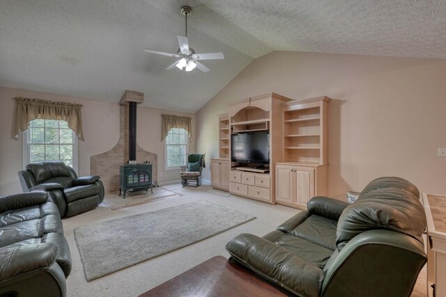 living room with a wood stove, a textured ceiling, ceiling fan, light colored carpet, and vaulted ceiling