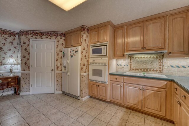 kitchen featuring light tile patterned flooring, a textured ceiling, tasteful backsplash, and white appliances