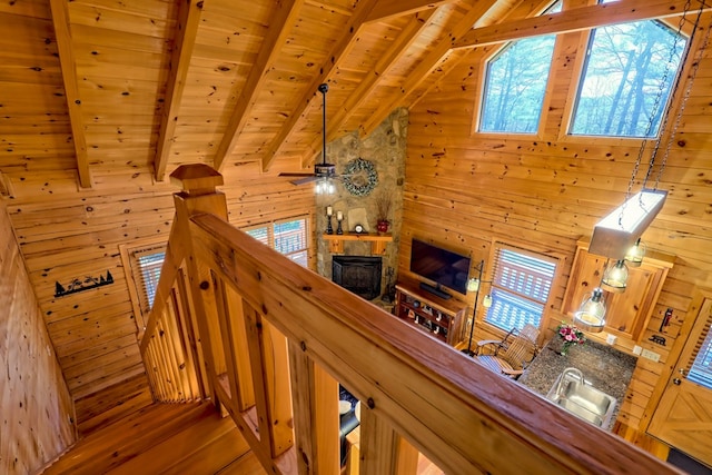 stairs with vaulted ceiling with beams, ceiling fan, wooden ceiling, wood walls, and a fireplace