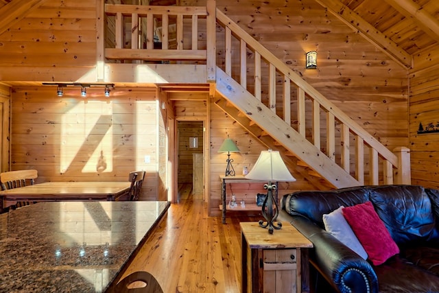 living area featuring light wood finished floors, lofted ceiling, wooden walls, wooden ceiling, and stairs