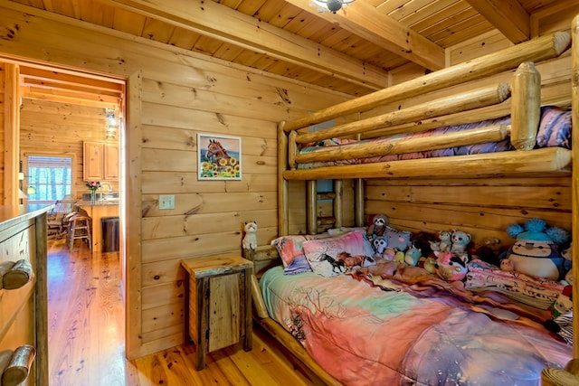 bedroom featuring wood walls, beam ceiling, and wood finished floors