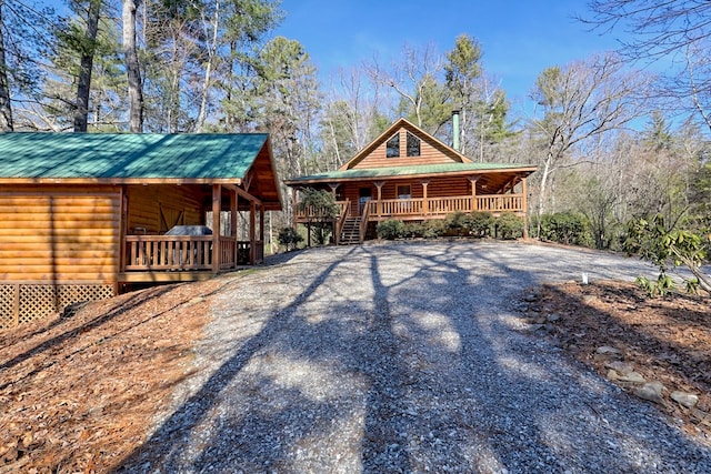 view of front of house featuring a porch, gravel driveway, log veneer siding, and metal roof