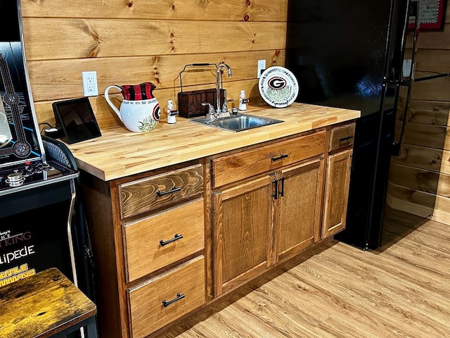 kitchen with wood counters, brown cabinetry, a sink, and freestanding refrigerator