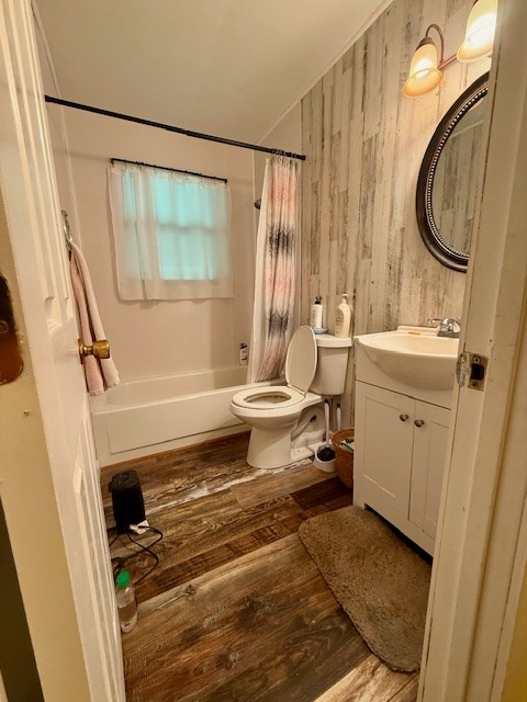 full bath featuring toilet, wood finished floors, vanity, wooden walls, and shower / bath combination with curtain