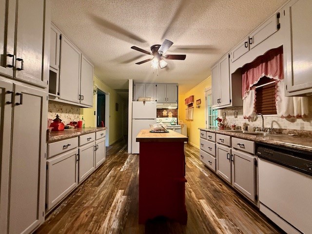 kitchen with a center island, a sink, ceiling fan, white appliances, and dark wood-style floors
