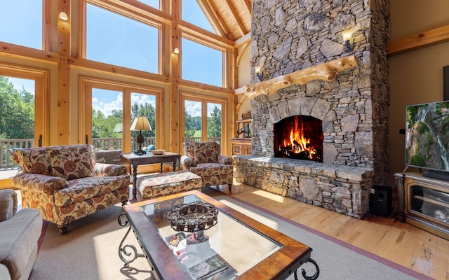 living room featuring high vaulted ceiling, a stone fireplace, and hardwood / wood-style flooring