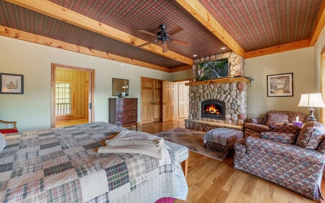 bedroom featuring ceiling fan, wooden ceiling, beam ceiling, a stone fireplace, and light wood-type flooring