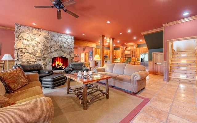 living room featuring a stone fireplace, ceiling fan, light tile flooring, and ornamental molding