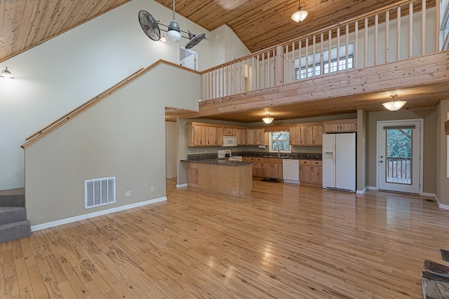 kitchen with white appliances, light hardwood / wood-style flooring, decorative light fixtures, and a towering ceiling