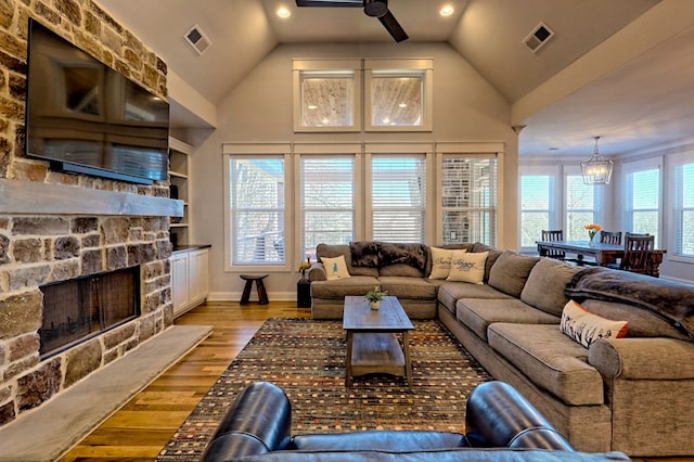 living room with a stone fireplace, light hardwood / wood-style flooring, high vaulted ceiling, and ceiling fan with notable chandelier