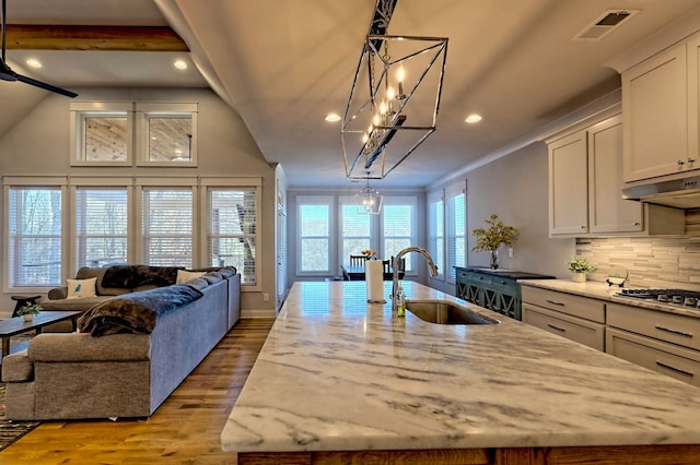 kitchen with sink, light stone countertops, an island with sink, decorative light fixtures, and stainless steel gas stovetop