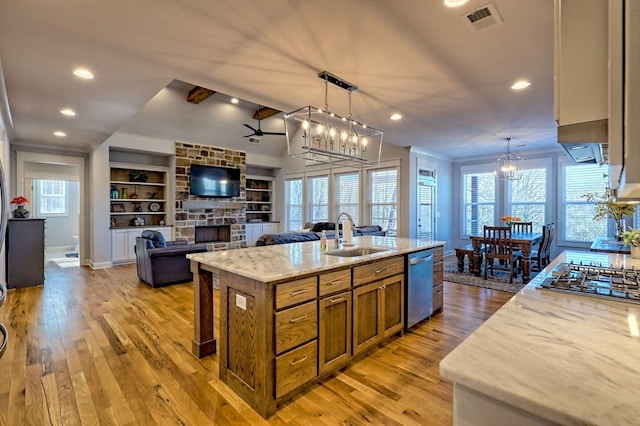 kitchen featuring sink, hanging light fixtures, a center island with sink, appliances with stainless steel finishes, and a fireplace