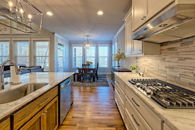 kitchen with appliances with stainless steel finishes, ventilation hood, sink, white cabinets, and light stone counters