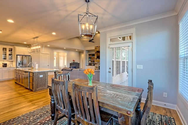 dining room with ornamental molding, a chandelier, vaulted ceiling, and light wood-type flooring