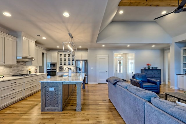 kitchen featuring a breakfast bar area, appliances with stainless steel finishes, a kitchen island with sink, pendant lighting, and light hardwood / wood-style floors