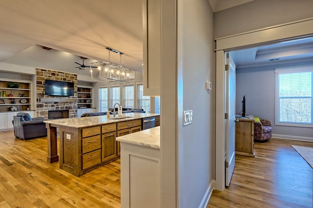 kitchen with sink, a stone fireplace, light stone counters, decorative light fixtures, and stainless steel dishwasher