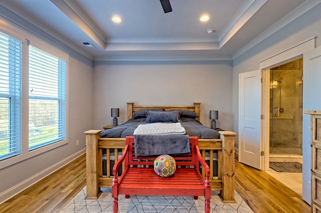 bedroom featuring light hardwood / wood-style floors, a raised ceiling, ceiling fan, and ensuite bathroom