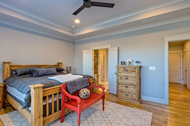 bedroom with a tray ceiling, ceiling fan, and light wood-type flooring