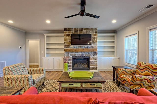 living room with crown molding, a fireplace, light hardwood / wood-style floors, and built in shelves