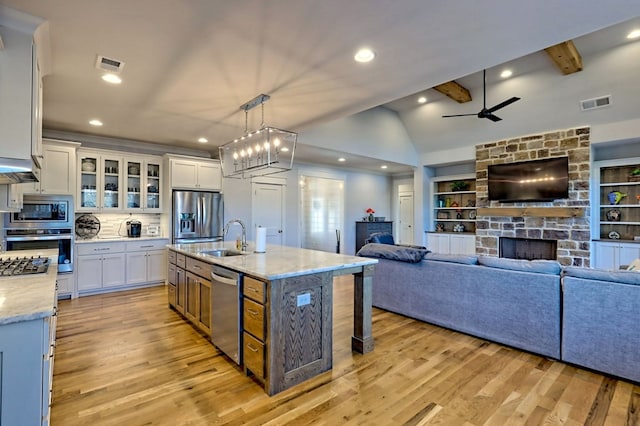 kitchen with appliances with stainless steel finishes, white cabinetry, a fireplace, light stone countertops, and a center island with sink