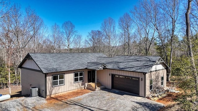 view of front of house featuring aphalt driveway, an attached garage, central AC, a shingled roof, and board and batten siding