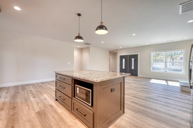 kitchen with light stone counters, visible vents, open floor plan, hanging light fixtures, and a center island