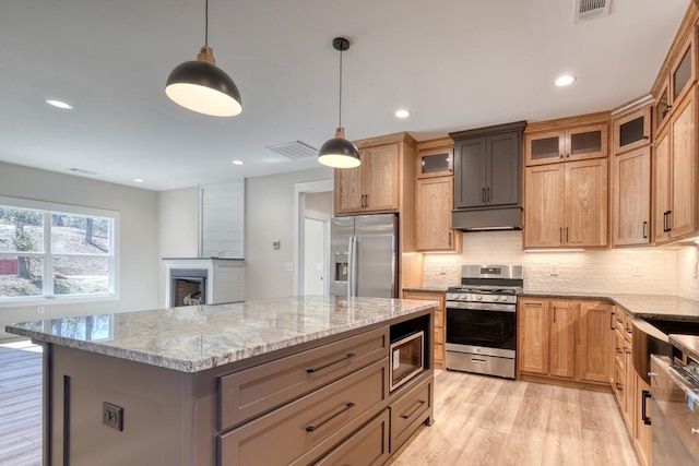 kitchen featuring light stone counters, a kitchen island, hanging light fixtures, appliances with stainless steel finishes, and glass insert cabinets