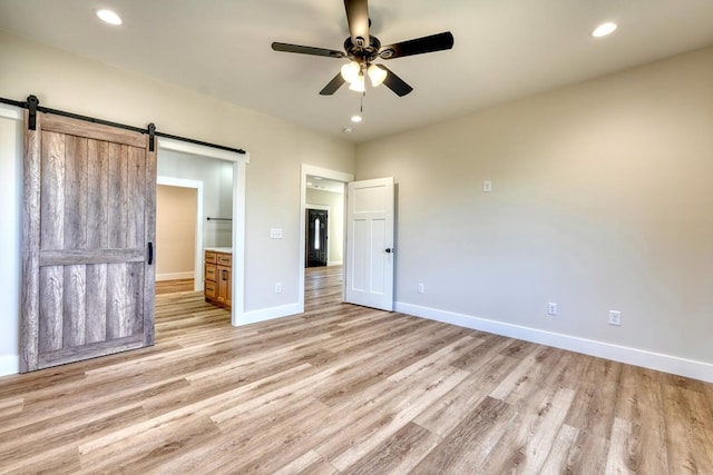 unfurnished bedroom with a barn door, recessed lighting, light wood-style flooring, and baseboards