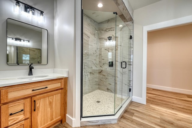 full bathroom with a stall shower, vanity, baseboards, and wood finished floors