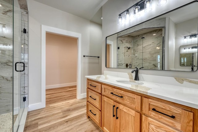 full bath with a marble finish shower, wood finished floors, vanity, and baseboards