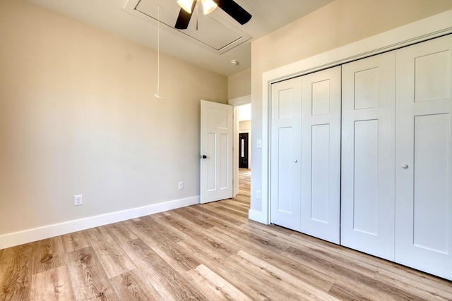 unfurnished bedroom with light wood finished floors, a closet, attic access, a ceiling fan, and baseboards