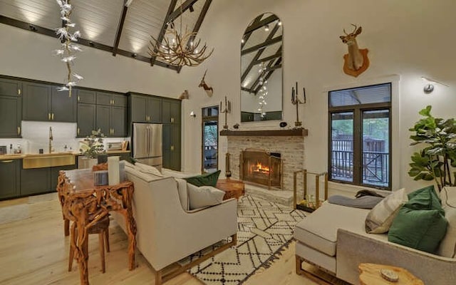 living room with a fireplace, light wood-type flooring, beam ceiling, sink, and a high ceiling