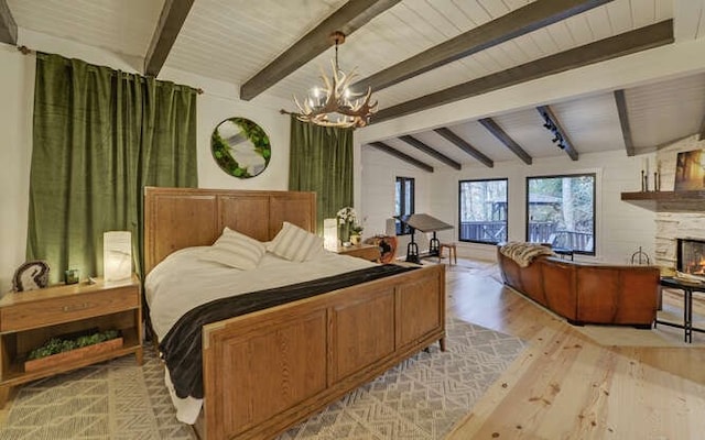 bedroom with a stone fireplace, lofted ceiling with beams, light hardwood / wood-style flooring, and a notable chandelier