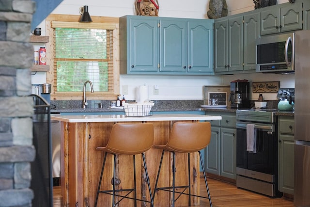 437 Spruce Cir, Mineral Bluff, GA 30559 - kitchen with stainless steel appliances, a kitchen bar, a sink, light wood finished floors, and blue cabinets