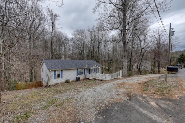 view of front of home featuring dirt driveway, a shingled roof, central AC unit, fence, and a view of trees