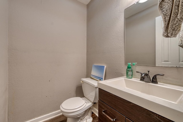 bathroom with a textured wall, vanity, toilet, and baseboards