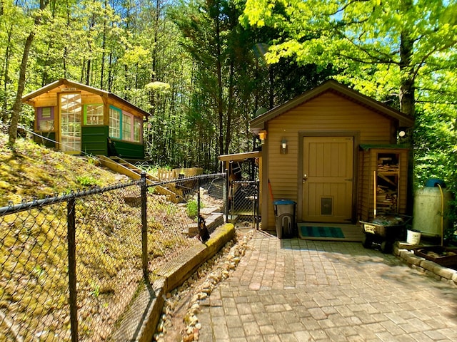 view of outbuilding with a gate, fence, a wooded view, and an outdoor structure