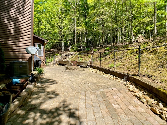 view of patio / terrace with fence, a view of trees, central AC, and an outdoor fire pit