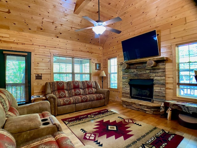 living room featuring ceiling fan, a stone fireplace, wood walls, high vaulted ceiling, and wood-type flooring