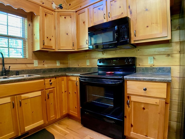 kitchen with a sink, light wood-style flooring, black appliances, and dark countertops