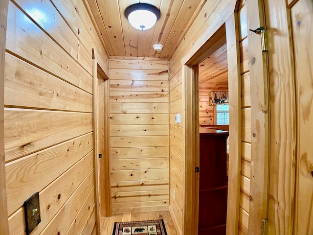 hallway with light wood-style floors, wood walls, and wooden ceiling