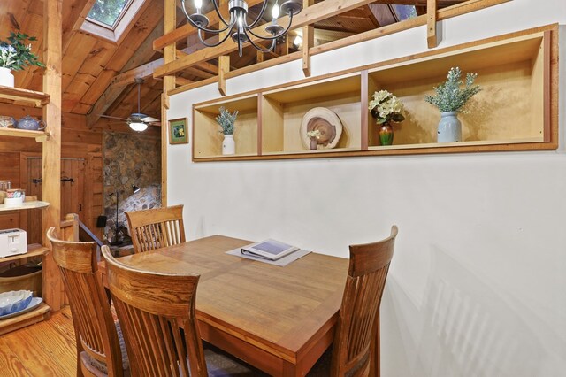 dining room featuring vaulted ceiling with skylight, ceiling fan with notable chandelier, wooden walls, and hardwood / wood-style floors