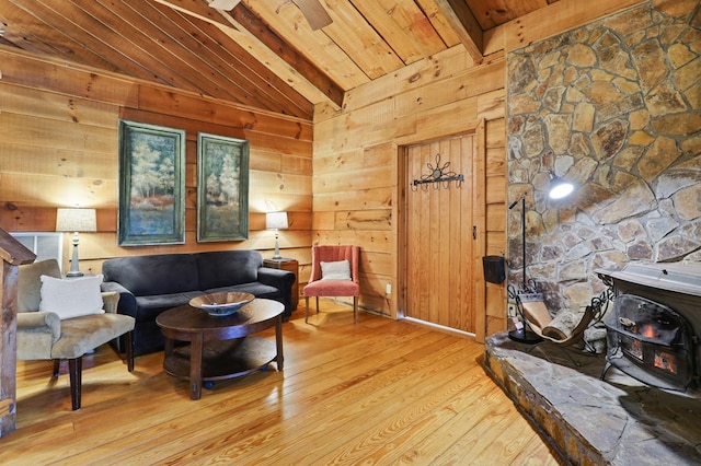 sitting room featuring light hardwood / wood-style floors, vaulted ceiling with beams, a wood stove, and wooden walls