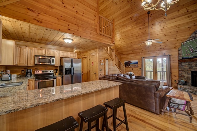 kitchen featuring sink, wooden walls, stainless steel appliances, french doors, and light stone counters